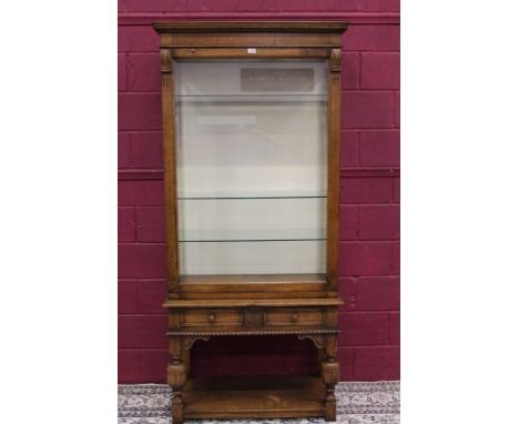 Good quality carved oak display cabinet with hinged bevelled glass front enclosing glass shelves between reeded columns, the 