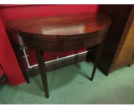 A Georgian style mahogany demi-lune card table the hinged fold over top on double gate square tapering legs