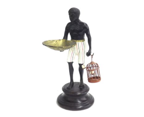 Cast bronze novelty pin tray in the form of a standing blackamoor holding a gilt scallop shell in one hand and a birdcage in 