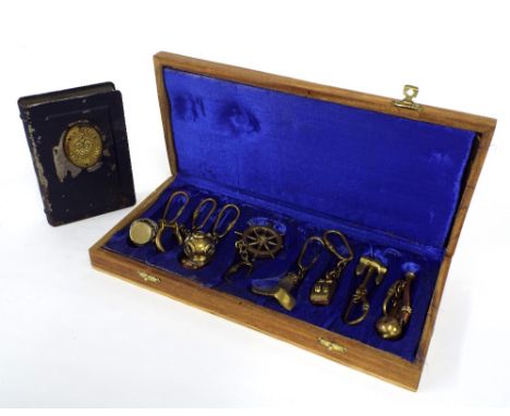 Interesting cased set of eight brass and copper charms of nautical interest to include lantern, ship's wheel, propeller, pull