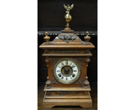 An early 20th century American oak cased Ansonia mantel clock, porcelain dial, Roman numerals, brass eagle finial, bronzed sp