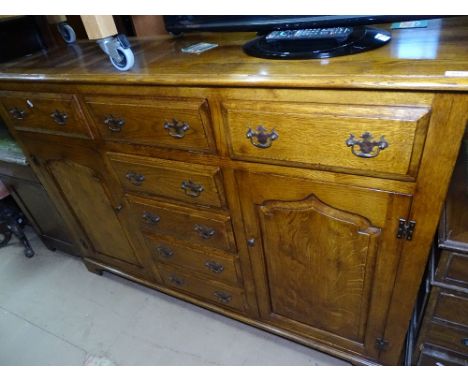 A good quality reproduction oak cabinet, with a central bank of drawers and fall fronts, flanked by fielded panelled cupboard