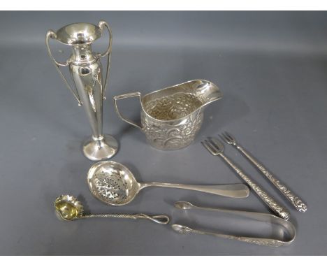 A silver hallmarked milk or cream jug with embossed foliate decoration, two pickle forks, a pair of sugar nips, a small ladle