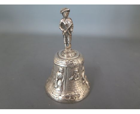 A silver hallmarked hand bell, the handle in the form of a figure playing Violin, the body decorated with figures in landscap