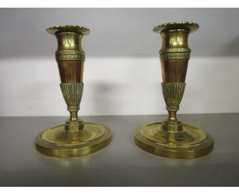 A pair of early 19th century French brass and copper candlesticks, decorated with banks of stiff leaves, arrow heads and alte