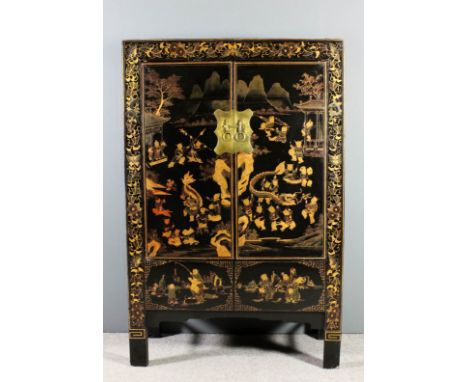 A Chinese black lacquer cabinet, fitted shelf enclosed by a pair of doors, decorated in gilt with children playing in a lands