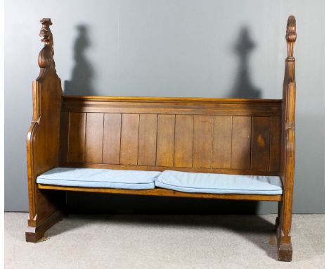 A Victorian oak church pew with moulded crest rail and panelled back, on shaped end supports, the tops boldly carved with an 