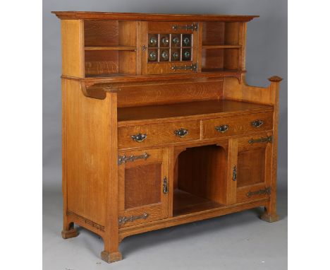 An Edwardian Arts and Crafts oak sideboard by Maple &amp; Co, the shelf back with a glazed cupboard, applied with overall pre