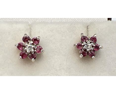 A pair of flower design ruby and diamond set stud earrings. Central round cut diamond surrounded by 6 small round cut rubies.