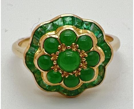 A 9ct gold emerald and jade dress ring in a fluted edge flower design by Luke Stockley, London. Set with a central green jade