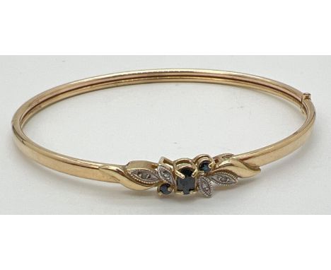 A gold sapphire and diamond set hinged bangle. Central oval cut sapphire with 2 small round cut sapphires and 4 small round c