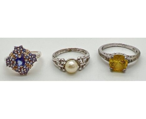 3 gem set silver dress rings. A central pearl ring with bow detail to shoulders; a clear stone and tanzanite set ring; and a 