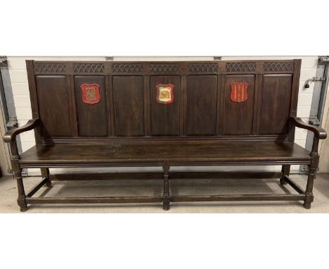 An antique dark wood high back settle bench with painted crest detail. Panelled back with carved Gothic detail, shaped arms a