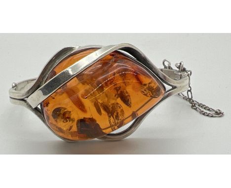 A modern design silver and Baltic amber bangle style bracelet with safety chain. Large central piece of amber with twist desi