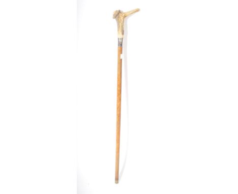 An early 20th walking stick cane having a carved bone handle resembling a pinocchio style character on a wooden shaft ending 