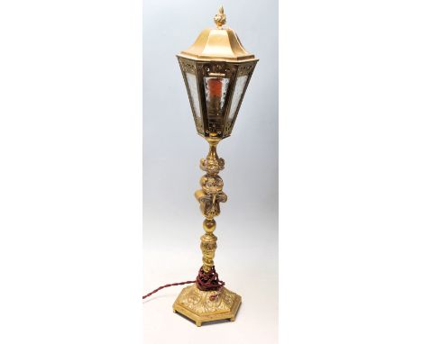 An early 20th Century brass desk lamp in the style of a Victorian street lamp having a fire shaped finial over a glass lanter