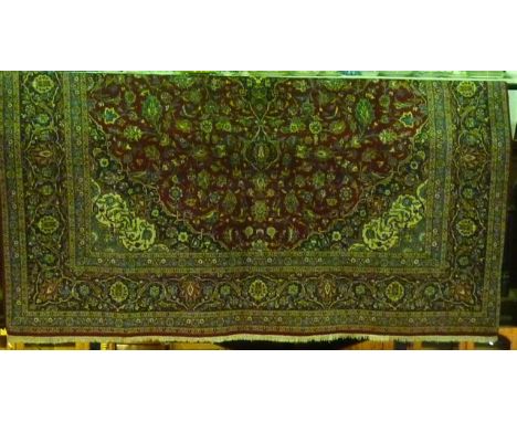 A Persian style wool carpet with floral detail upon a red field within wide banded running borders
