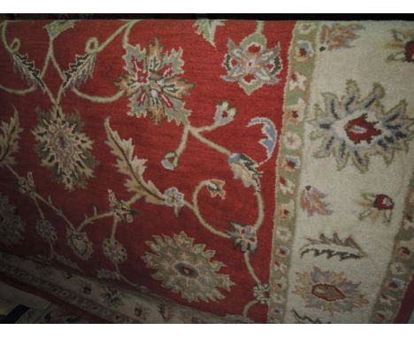A Persian style wool carpet with brick red field, scrolling floral decoration, set within wide banded borders