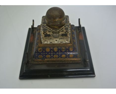 A 19th century inkstand raised on a square ebonised base with gilt brass and enamelled centre supporting a cut glass inkwell 