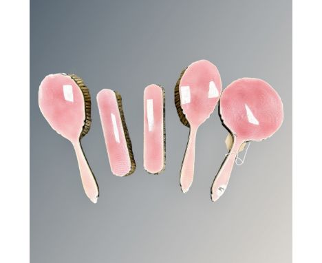 An five-piece enamel and silver dressing table set, with rose pink guilloche enamel, comprising four hand brushes and a hand 