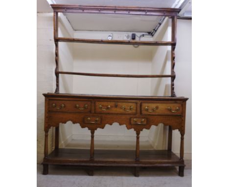 A George III oak dresser, having a moulded cornice, over two shelves with shaped ends, the base comprising three in-line and 