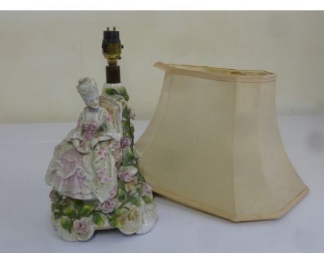 A porcelain table lamp in the form of a lady in 18th century costume and with pink silk shade