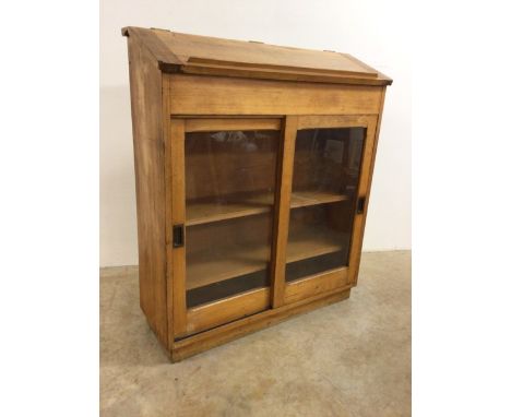 A light oak library bookcase with double sliding glazed doors and brass handles also with hinged book slope to interior stora