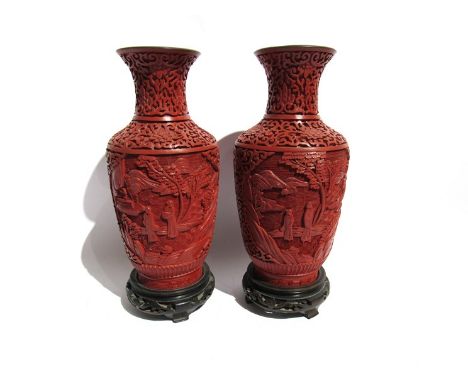 A near pair of Chinese red cinnabar lacquer vases decorated with figures in garden, blue enamel interiors, on wooden stands, 