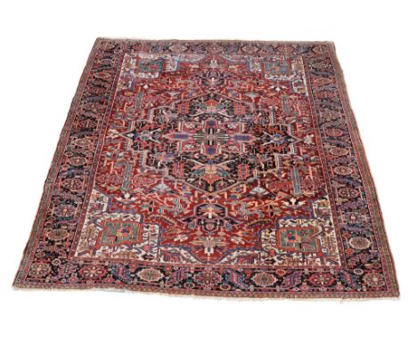  A Heriz carpet,   decorated with abstracted foliate motifs throughout, the central navy medallion within a madder field and 