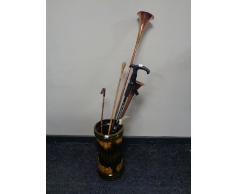 A glazed ceramic stick stand containing copper and brass hunting horns, riding crop, walking stick etc  