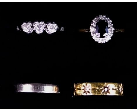 Four 18ct Gold Rings, comprising - three stone diamond heart ring, size K, white gold wedding band, size H, gem set eternity 