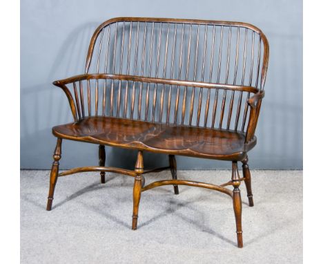 A Dark Elm Windsor Stickback Two-Seat Bench/Settle, with dished wood seat on turned legs with twin crinoline stretchers,&nbsp
