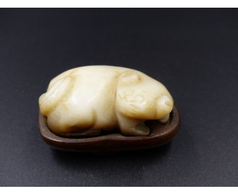 A CHINESE CARVED JADE SMALL FIGURE OF A PUPPY ON A HARDWOOD BASE.   L.4.5cms.