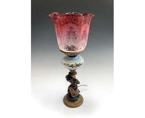 A late 19th century painted spelter and glass figural oil lamp, converted to electricity, with etched cranberry glass shade. 