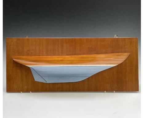 A half hull model of a boat, possibly a Kim Holman design, mounted on a wooden plaque. The plaque 32 x 78.5cm. 