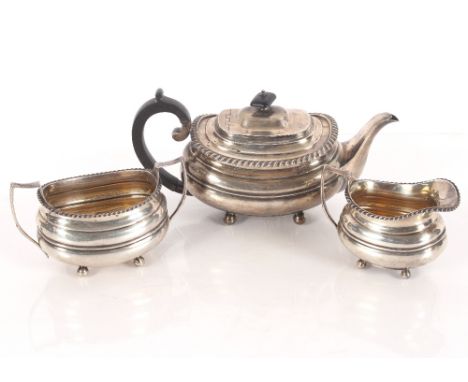 A George V silver tea set, of cushion shape with gadrooned border raised on ball feet, the teapot with black wood handle and 