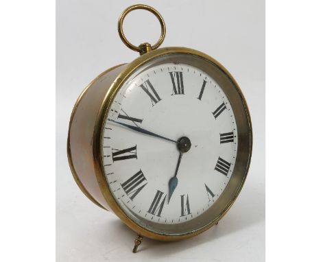 A circular brass cased clock, the white enamel dial with Roman numerals with circular case, ring handle and raised on two spi