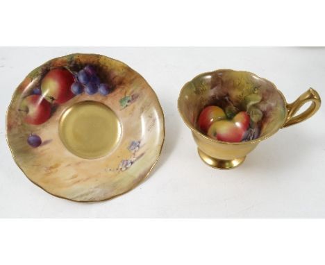 A Royal Worcester pedestal tea cup and saucer, the interior of the cup and saucer hand painted with fruit to a mossy backgrou