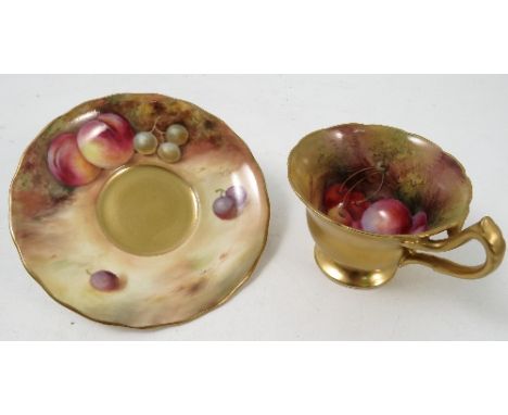A Royal Worcester pedestal tea cup and saucer, the interior of the cup and saucer hand painted with fruit to a mossy backgrou