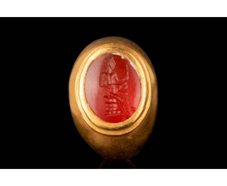 Ca. AD 100 - 200. An oval-shaped carnelian intaglio engraved with a nude male figure seated atop a pile of rocks. He holds a 
