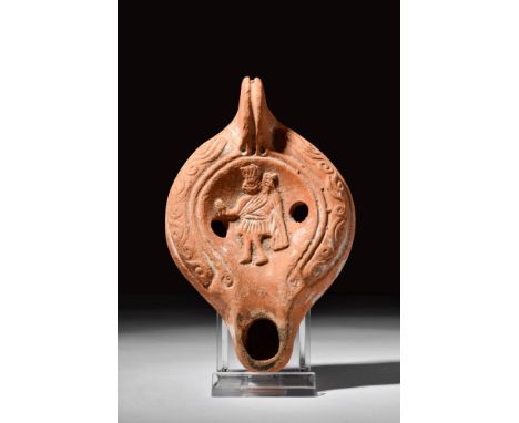 Ca. AD 200 - 300. A terracotta oil lamp with a rounded body and a central relief depicting a man in a short toga. He is holdi