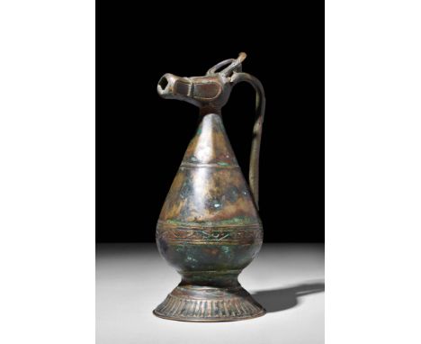 Ca. AD 1100 - 1200. A bronze ewer with a piriform body resting atop a flared foot with a ribbed edge. The spout is modelled i