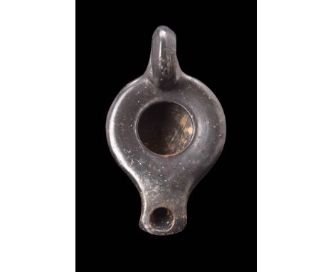 Ca. 400 - 300 BC. A Greek black glazed terracotta oil lamp, with a flat rounded body with a large central filling hole. The l