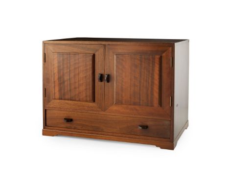 COTSWOLD SCHOOL WALNUT TABLE CABINET, CIRCA 1930the twin cupboard doors above a long drawer, the whole raised on a plinth bas