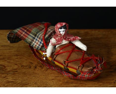 An unusual glazed china shoulder head miniature doll, stuffed cloth body, wearing a red and white floral-patterned head cloth