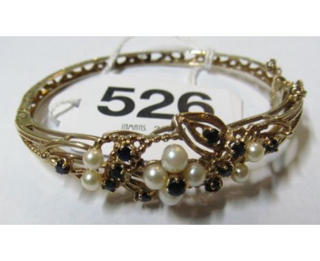 A gold coloured bangle set pearls and blue stones