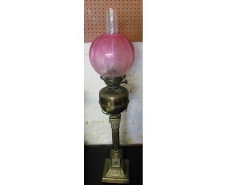 A brass oil lamp on column base with pink glass shade