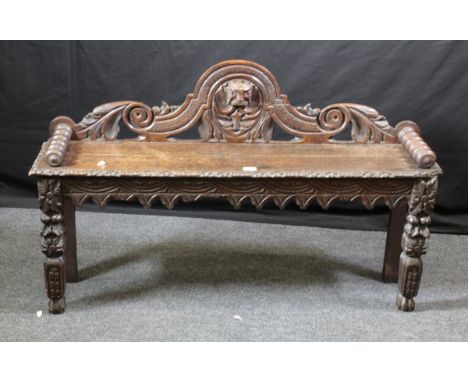 A Victorian oak hall seat, having an arched, scroll and mask carved back, bobbin turned arms, wavy fluted and arcaded frieze,