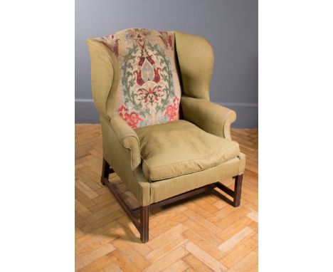 A Chippendale style hipped wing back fireside armchair with needlepoint worked back, raised on square section mahogany under 