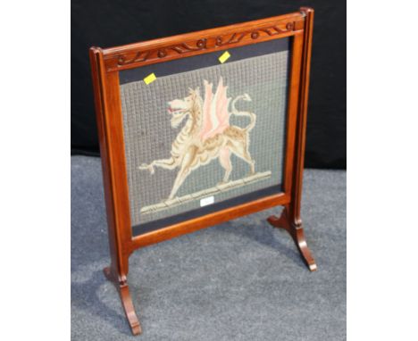 An Edwardian mahogany firescreen, decorated with a gros point woolwork of a Welsh dragon beneath a blind fret frieze, on spla